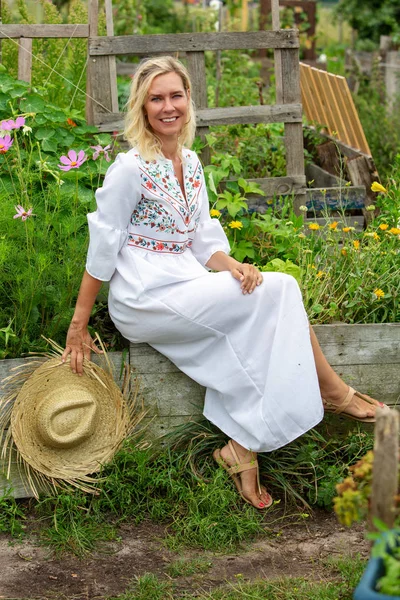 Bella donna bionda in abito bianco seduta fuori in giardino — Foto Stock