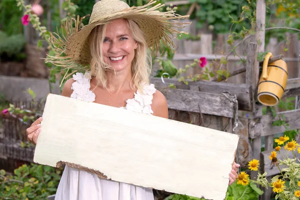 Donna bionda in piedi in giardino e con in mano un segno di legno — Foto Stock