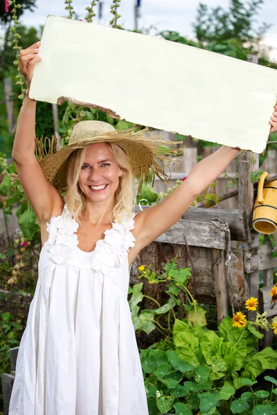 Donna bionda in piedi in giardino e con in mano un segno di legno — Foto Stock