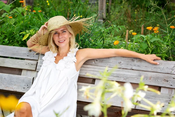 Bella donna bionda in abito bianco seduta fuori in giardino — Foto Stock