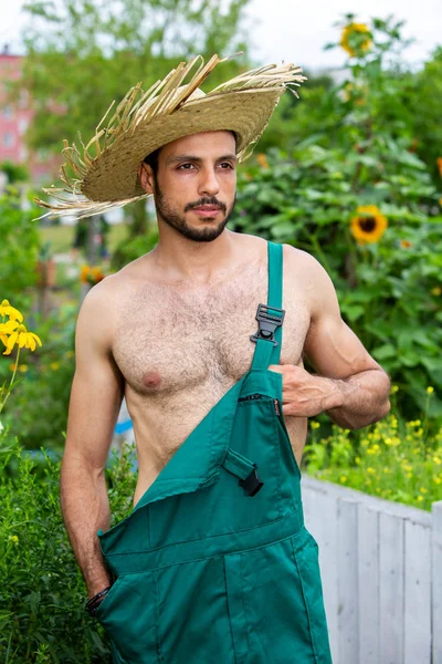 Handsome gardener with green pants and straw hat standing in gar — Stock Photo, Image