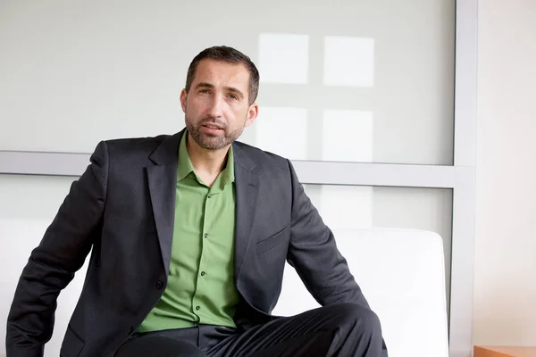 Kjekk forretningsmann i dress og grønn skjorte som sitter innendørs – stockfoto