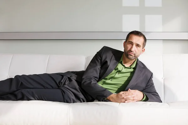 En kjekk forretningsmann i dress som ligger på sofaen og slapper av – stockfoto