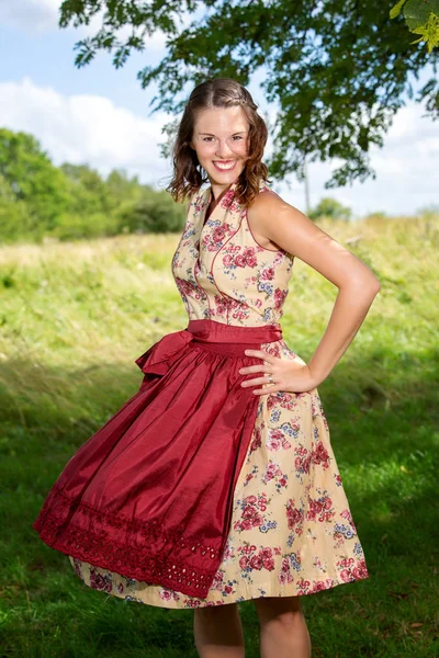 Mujer joven en dirndl de pie al aire libre junto a un árbol —  Fotos de Stock