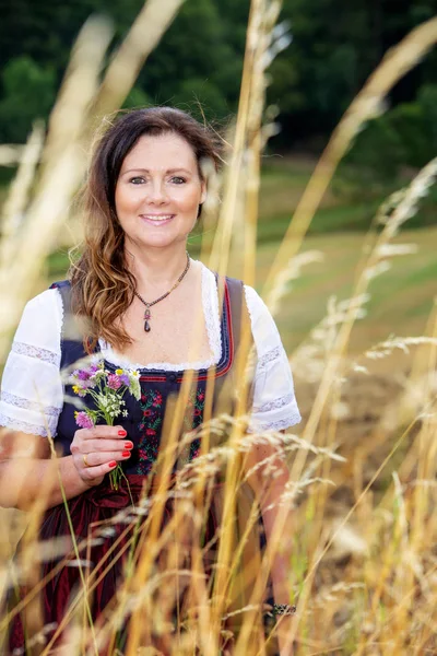 Brunette vrouw in Dirndl staande buitenshuis en houden van bloemen — Stockfoto