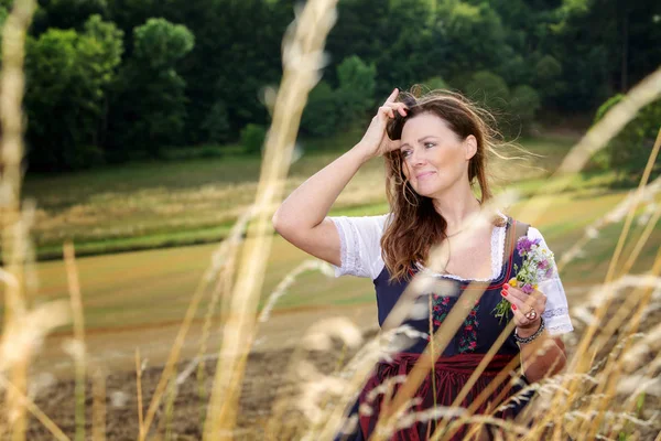 Morena mujer en dirndl de pie al aire libre y sosteniendo flores —  Fotos de Stock