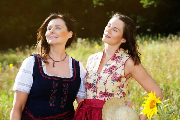 Dos mujeres en dirndl bavariana de pie al aire libre y disfrutando de la —  Fotos de Stock