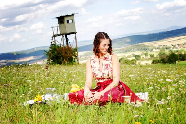 Jonge brunette vrouw in Dirndl zittend in een veld van bloemen op — Stockfoto