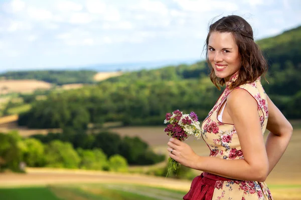 Woman in dirndl standing outdoors and holding flowers — Stock Photo, Image