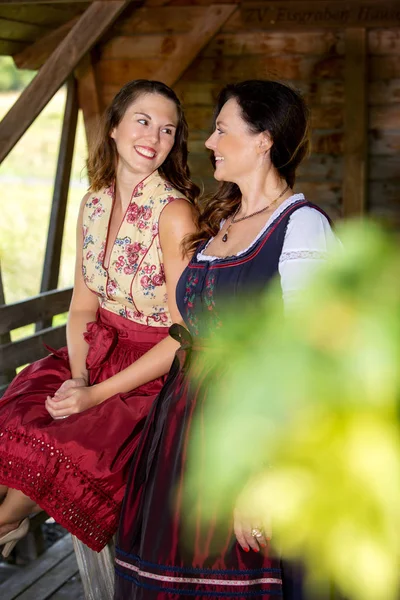 Zwei bayrische Frauen im Dirndl vor einer Holzhütte — Stockfoto