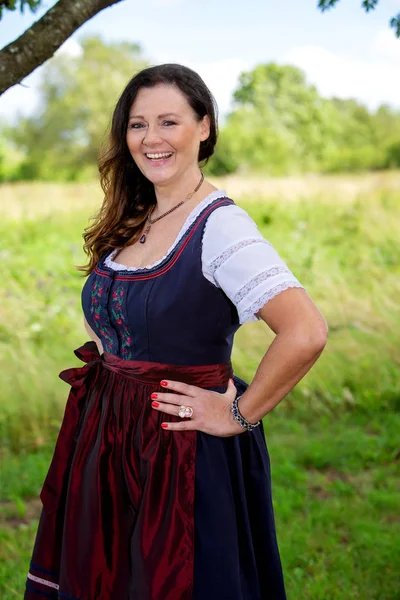 Brunette vrouw in Dirndl staande buiten door een boom — Stockfoto