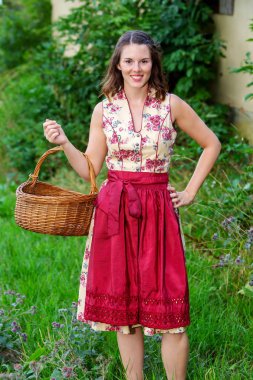 dirndl genç kadın çiftlik evinde ayakta ve sepet tutan