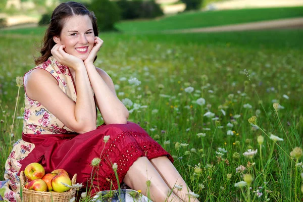 上の花のフィールドに座ってダーンドルの若いブルネットの女性 — ストック写真
