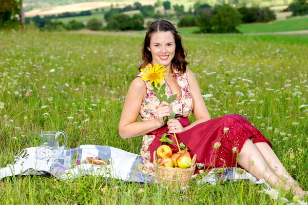 Mujer joven en dirndl sentado en el prado y la celebración de girasol — Foto de Stock
