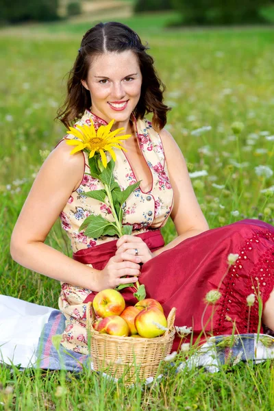 Mujer joven en dirndl sentado en el prado y la celebración de girasol — Foto de Stock