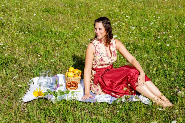 Jonge brunette vrouw in Dirndl zittend in een veld van bloemen op — Stockfoto