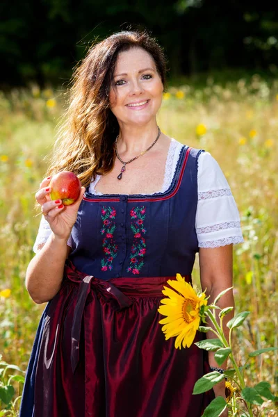 Mulher em dirndl no campo de flores segurando uma maçã — Fotografia de Stock