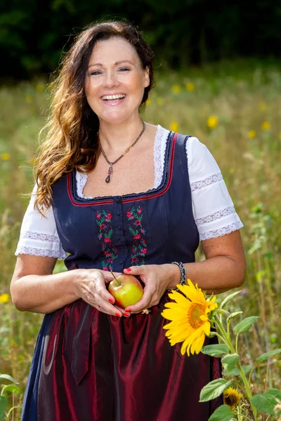 Mujer en dirndl en campo de flores sosteniendo una manzana —  Fotos de Stock