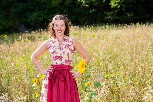 Jonge vrouw in Dirndl staande in het veld van bloemen — Stockfoto