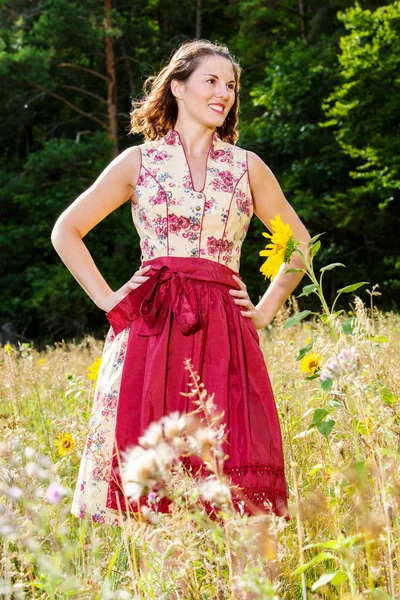 Jonge vrouw in Dirndl staande in het veld van bloemen — Stockfoto