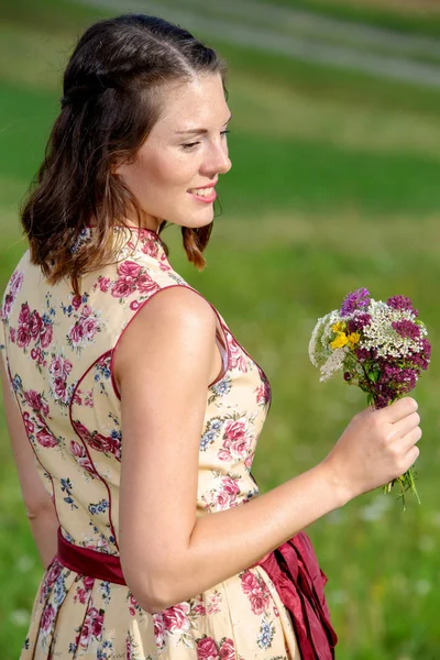 Νεαρή γυναίκα σε φουστίτσα στέκεται έξω και κρατώντας λουλούδια — Φωτογραφία Αρχείου