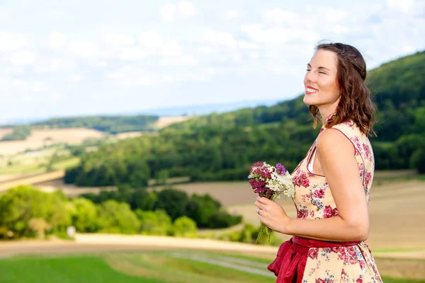 年轻的女人在迪恩德尔站在草地上与鲜花和享受 — 图库照片