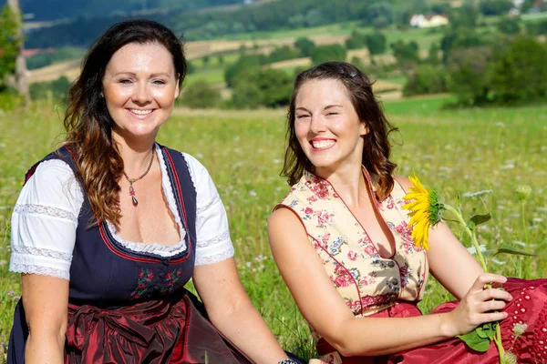 Due donne in Dirndl seduti su una coperta nel prato e ridendo — Foto Stock