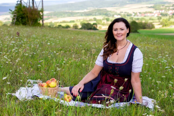 Vrouw in Dirndl zittend op deken in weide — Stockfoto