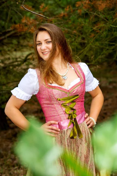 Mujer joven en dirndl de pie junto al árbol y sonríe — Foto de Stock