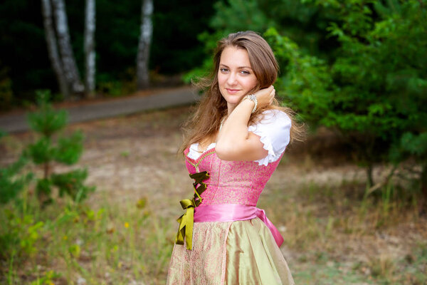 young woman in dirndl standing in forest and smiles