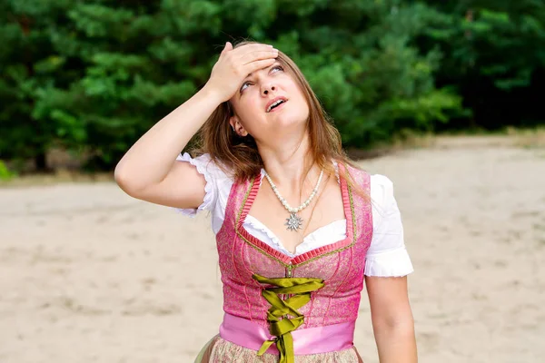 Jovem mulher em dirndl de pé ao ar livre e tendo uma dor de cabeça — Fotografia de Stock