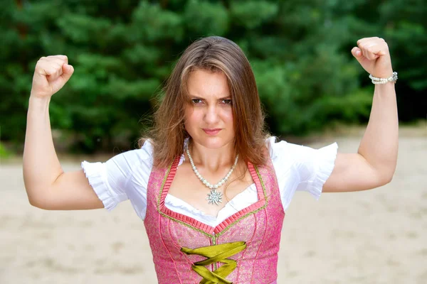 Jovem mulher em dirndl de pé ao ar livre e flexionando seus músculos — Fotografia de Stock