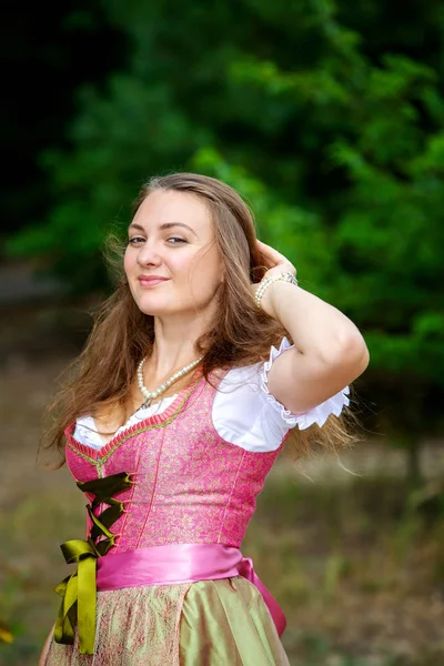 Joven mujer en dirndl de pie en el bosque y sonrisas —  Fotos de Stock