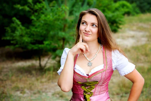 Jonge vrouw in Dirndl staande buitenshuis en op zoek Rosy — Stockfoto