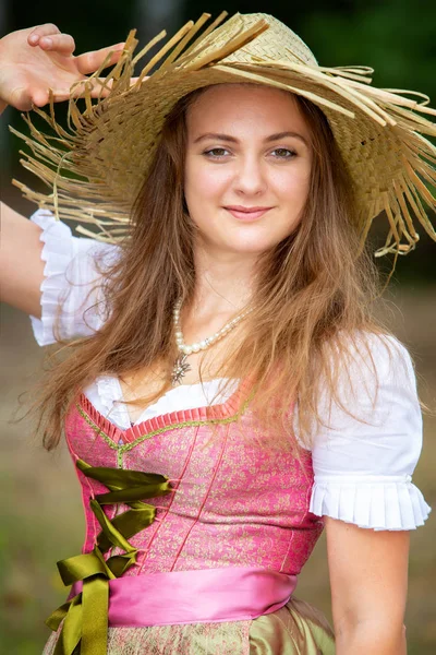 Mujer joven en dirndl y sombrero de paja de pie al aire libre —  Fotos de Stock