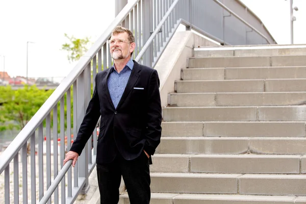 Bonito empresário sorrindo e de pé por escadas — Fotografia de Stock