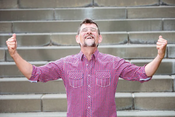 Gutaussehender Mann Mitte 50 hebt die Arme und sieht glücklich aus — Stockfoto