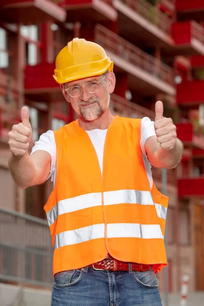 Trabajador guapo con casco en sus 50 años sosteniendo pulgares hacia arriba —  Fotos de Stock