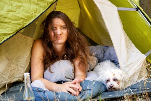 Junge Frau liegt mit ihrem weißen Hund im Zelt und sieht müde aus — Stockfoto