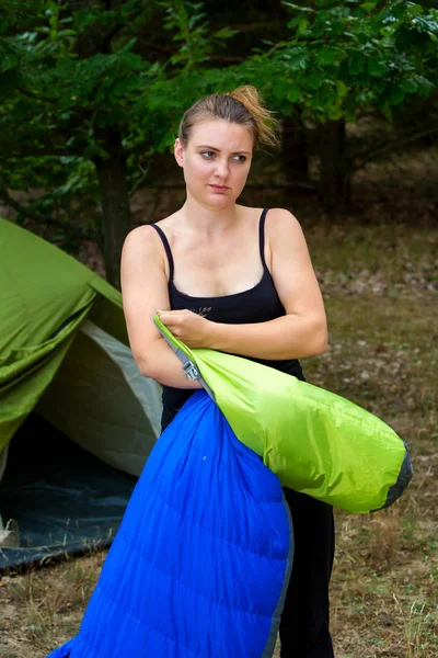 Mujer joven en frente de la tienda de campaña embalaje de su saco de dormir — Foto de Stock