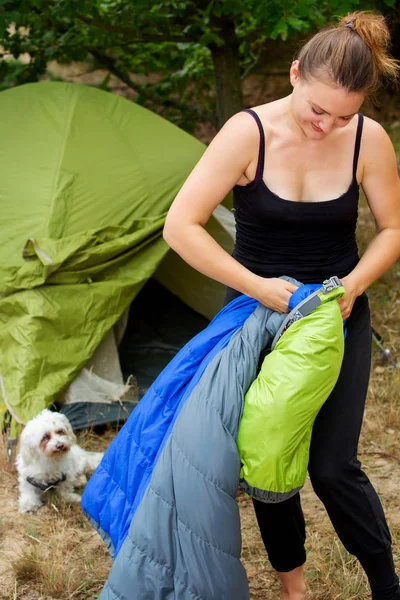 Giovane donna davanti alla tenda disimballando il suo sacco a pelo — Foto Stock