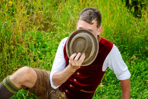 Bajor férfi ül a fűben, és mögé bújva a kalapját — Stock Fotó