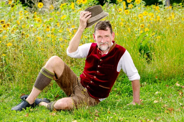 Knappe Beierse man zitten in de voorkant van het veld van zonnebloemen — Stockfoto