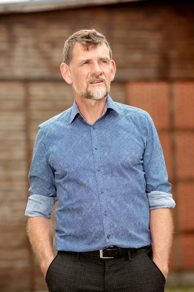 Knappe man in zijn 50s in blauw shirt staande buiten — Stockfoto