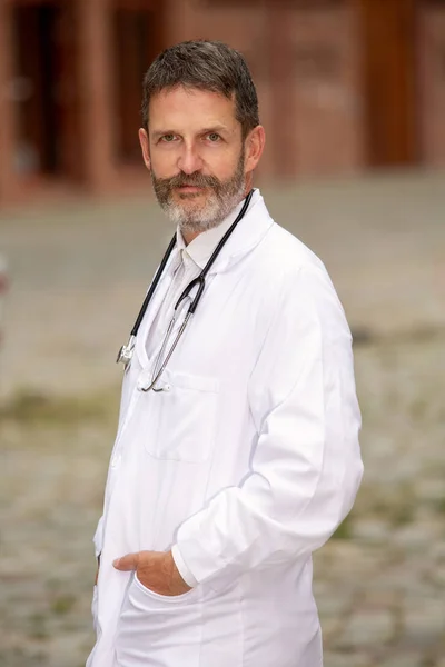 Bello medico barbuto in camice bianco in piedi al di fuori — Foto Stock