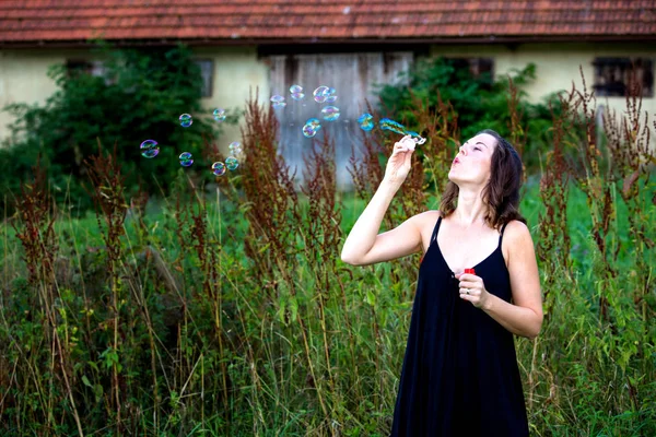 Jovem morena de pé ao ar livre e soprando bolhas de sabão — Fotografia de Stock