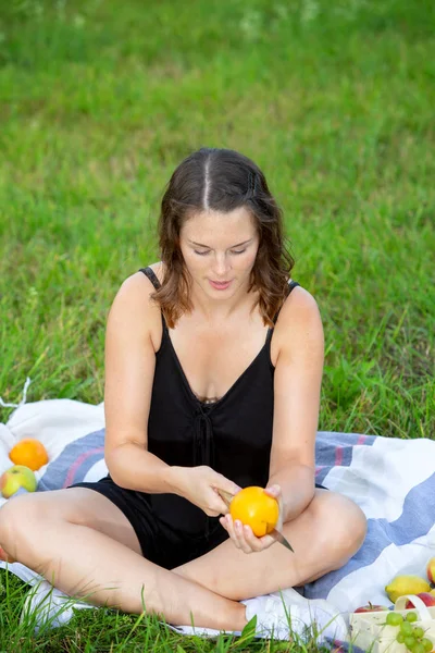 Giovane donna seduta nel parco e tagliando un'arancia — Foto Stock