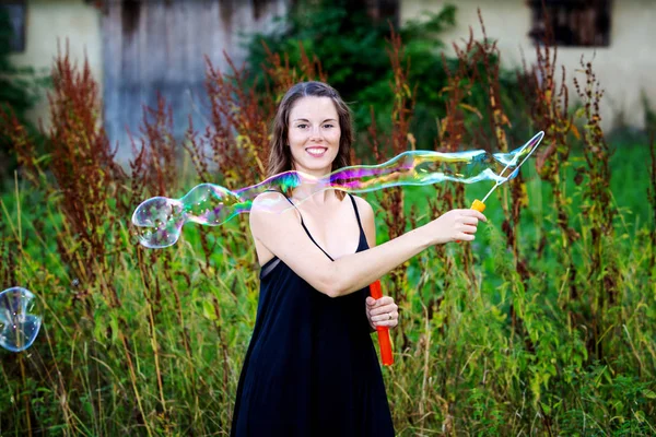 Joven morena mujer de pie al aire libre y soplando burbujas de jabón —  Fotos de Stock