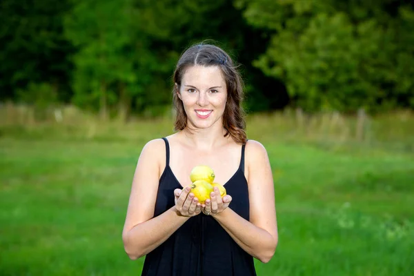 Молодая женщина стоит на открытом воздухе в природе и держит лимоны — стоковое фото