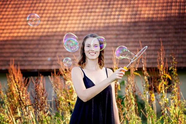 Joven morena mujer de pie al aire libre y soplando burbujas de jabón —  Fotos de Stock
